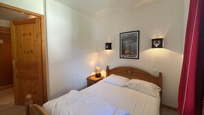 A bedroom with a wooden bed, white bedding, a nightstand with a lamp, and a poster on the wall.