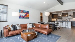 A modern living room with a leather sectional sofa, a coffee table, and a vibrant abstract painting. - Eagle Lodge Shuttle | Mountain Views (Mammoth Lakes)