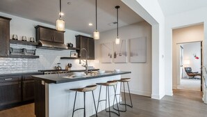 A modern kitchen with a large island, bar stools, pendant lighting, and dark cabinetry. - Eagle Lodge Shuttle | Mountain Views (Mammoth Lakes)