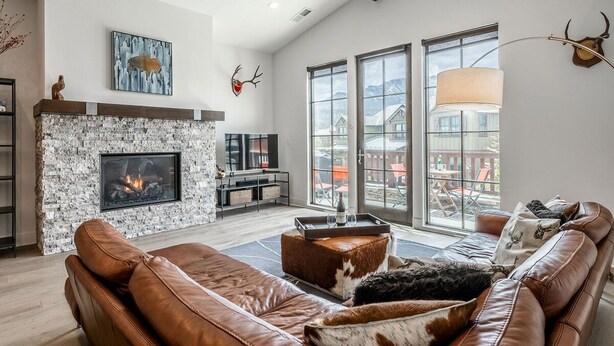 A spacious living room with a stone fireplace, leather sofas, and large windows offering a view of the outdoors. - Eagle Lodge Shuttle | Mountain Views (Mammoth Lakes)