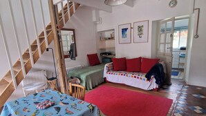 A cozy room with a wooden staircase, a dining table with a colorful tablecloth, a red rug, and a sofa. - Small house on the marina. (Pontrieux)