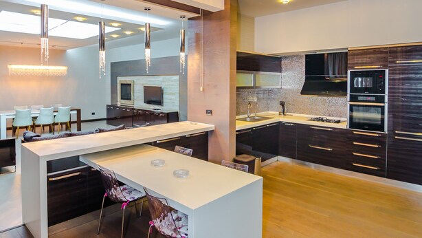 A modern kitchen with a central island, wooden flooring, and contemporary lighting fixtures.