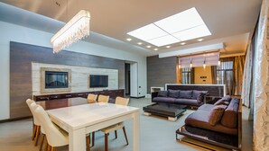 A modern living room with a dining area, a sofa set, and a TV mounted on the wall.
