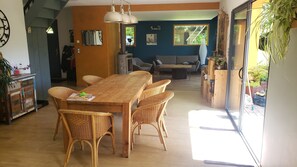 A dining area with a wooden table and wicker chairs, a kitchen area with a stove, and a view through a glass door to an outdoor space.