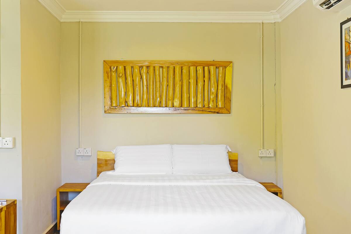 A neatly made bed in a room with a large, golden artwork above it.