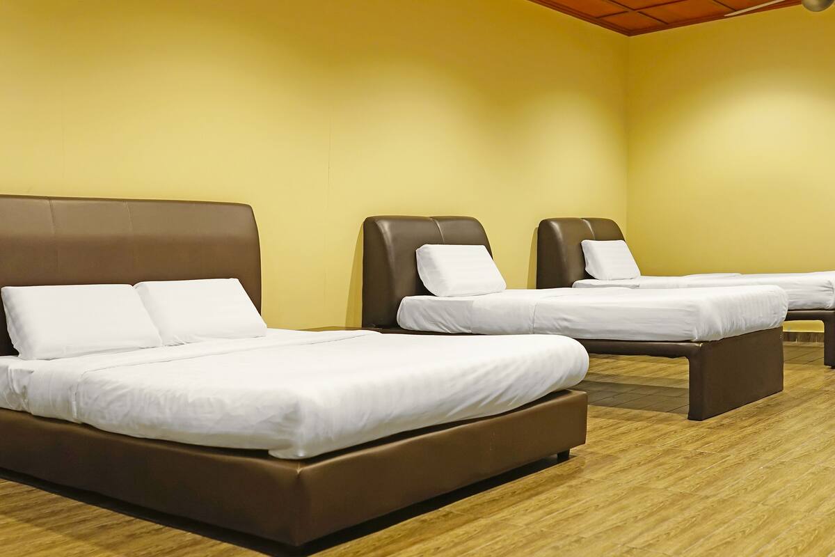 A hotel room with three beds, each with white bedding and brown headboards.