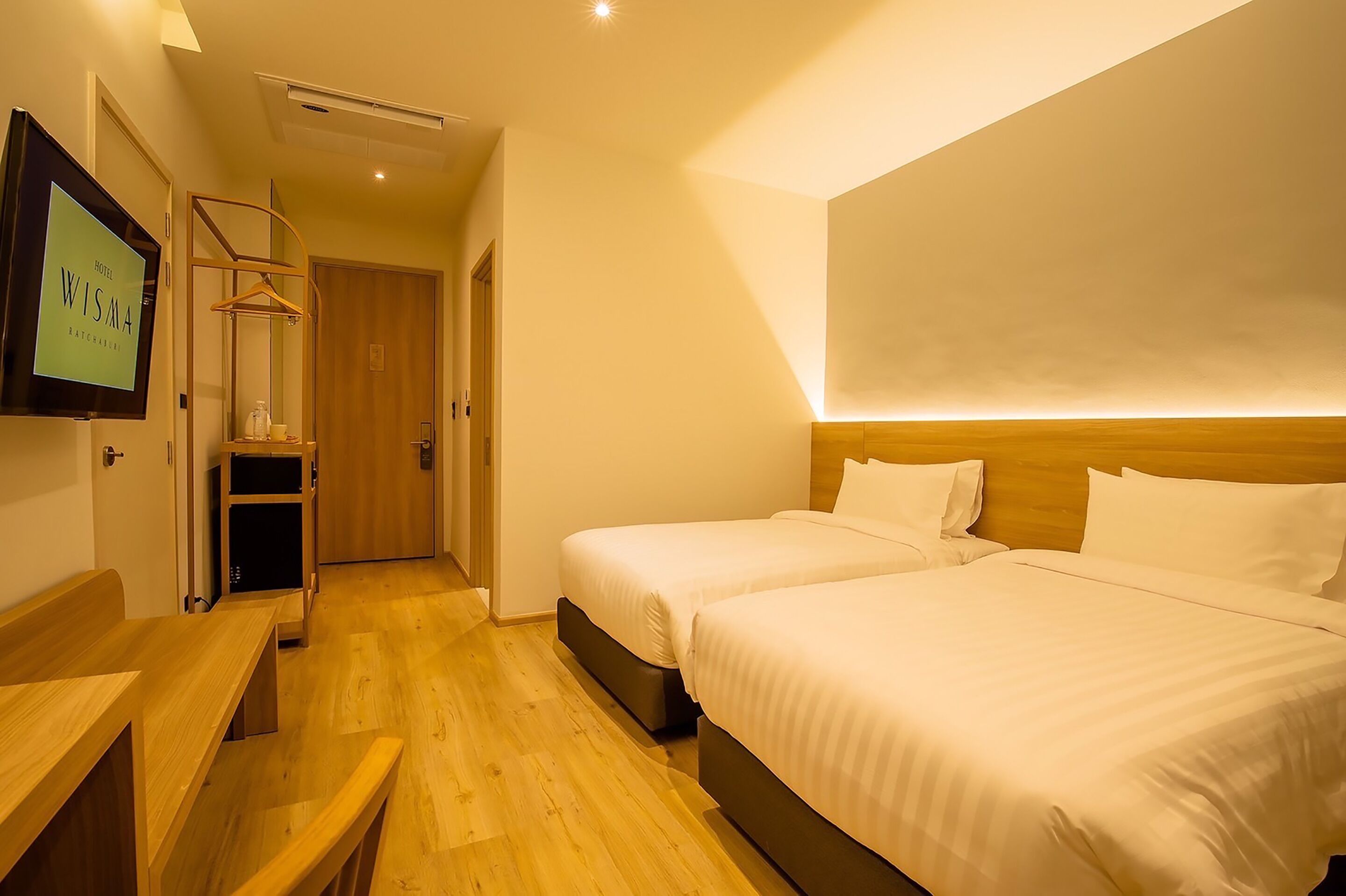 Habitación de hotel con dos camas, un banco de madera, un televisor y una puerta de madera.