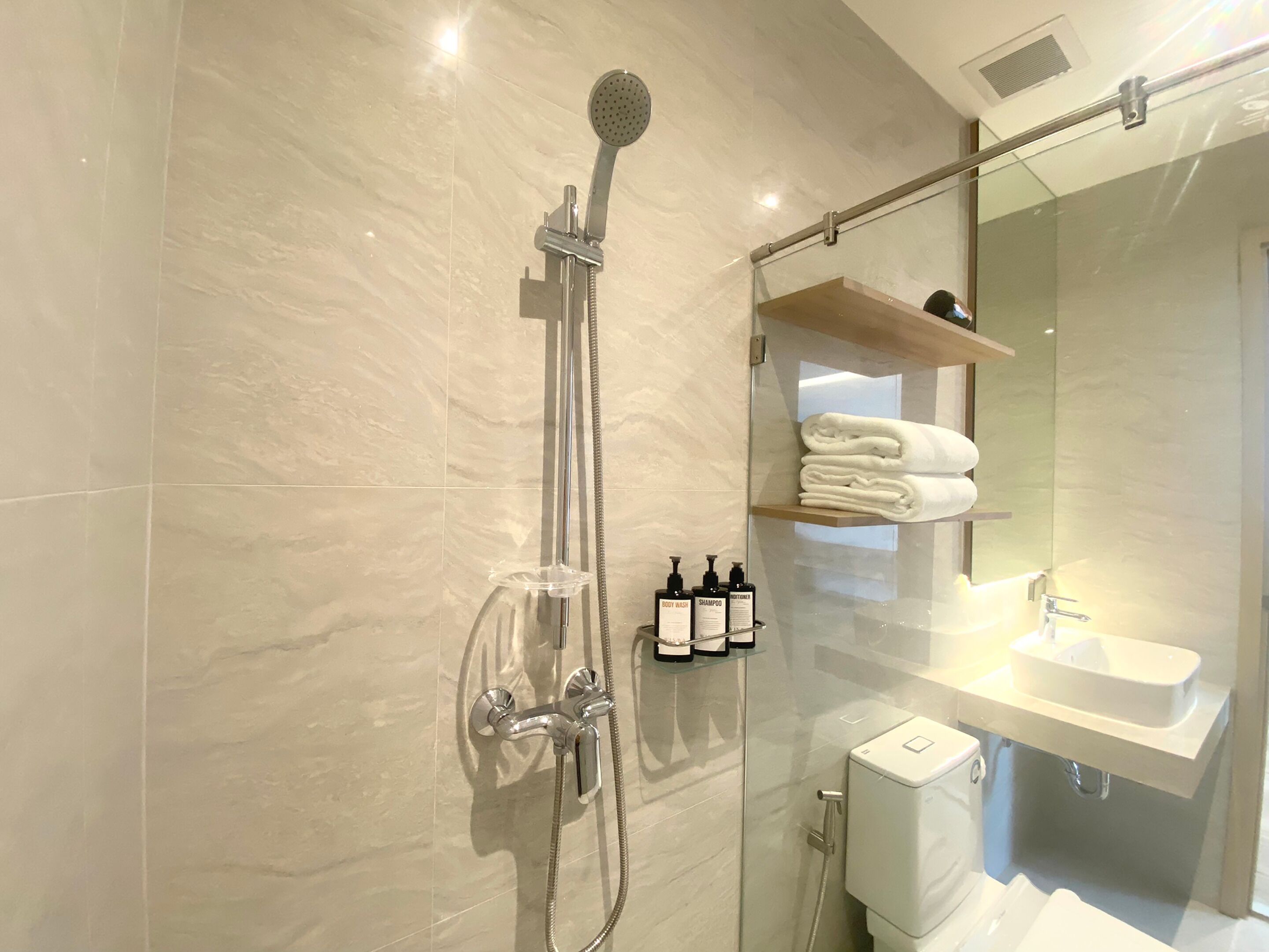 A modern bathroom with a glass-enclosed shower, a white toilet, and a sink with a mirror above it.