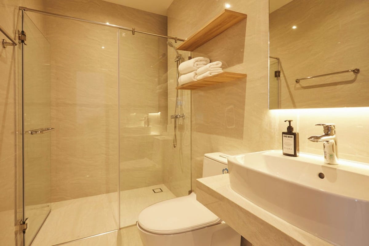 A modern bathroom with a glass-enclosed shower, a white toilet, and a sink with a soap dispenser.