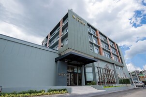Un hotel moderno con un llamativo letrero “WISAA”, una entrada amplia con puertas de vidrio y una estructura de varios pisos con balcones visibles.