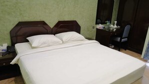 Una cama bien hecha con sábanas blancas en una habitación con paredes verdes y un cabecero de madera oscura.