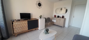 Un espacio habitable compacto con televisión, refrigerador pequeño, mesa de comedor y zona de estar.