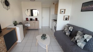 Ein modernes Wohnzimmer mit einer Couch, einem Couchtisch, einem Fernseher, einer Küchenzeile inklusive Waschmaschine und einem Esstisch mit Stühlen.