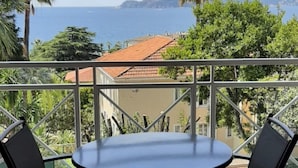 Ein Balkon mit rundem Tisch und zwei Stühlen, mit Blick auf eine Küstenlandschaft mit Palmen und Gebäuden.