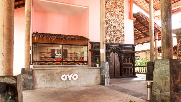 A reception area with a counter labeled "OYO," a stone wall, and a traditional wooden door. - Collection O Ivory Hotel & Resort (Rawang)