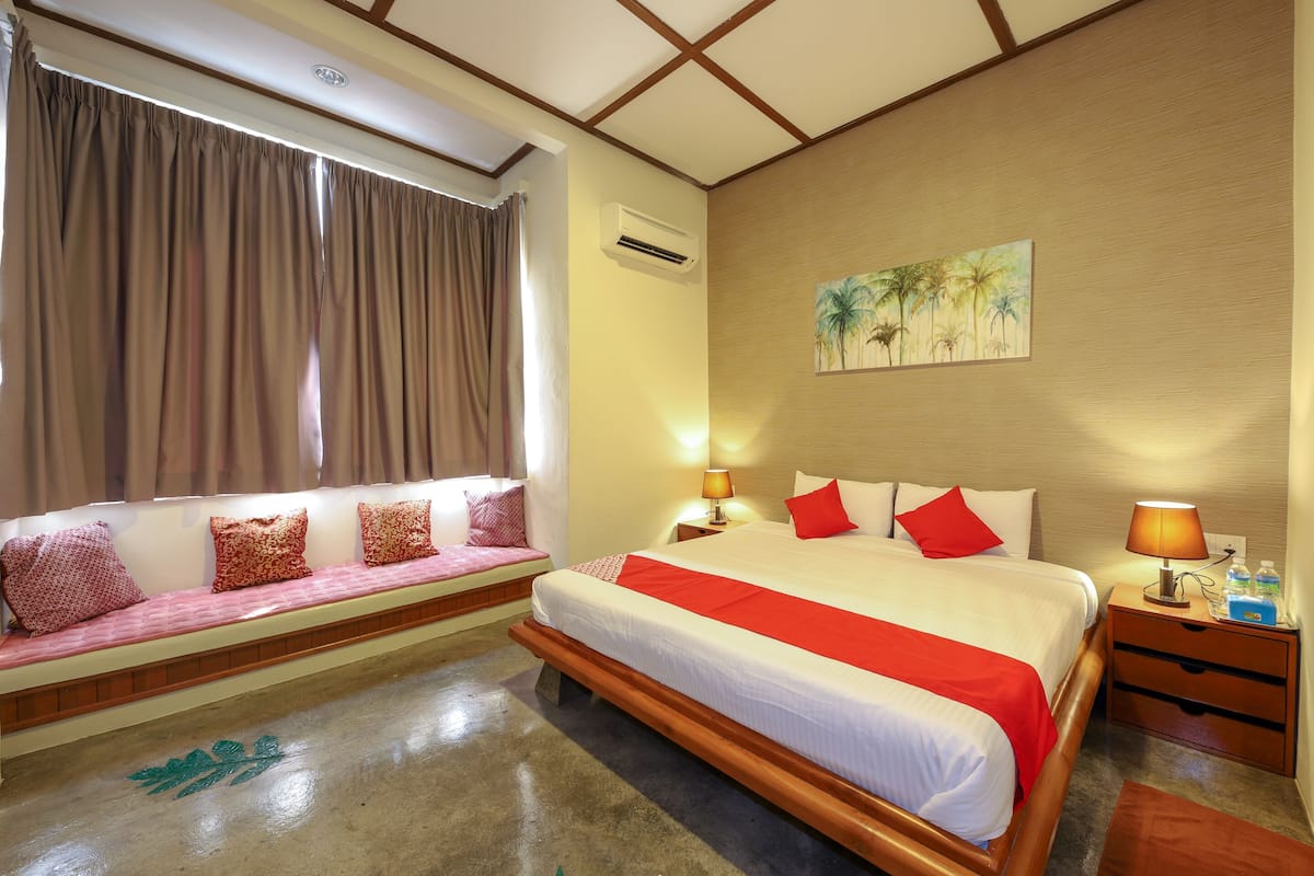 A hotel room with a bed, a bench with cushions, a nightstand with a lamp, and a painting on the wall.