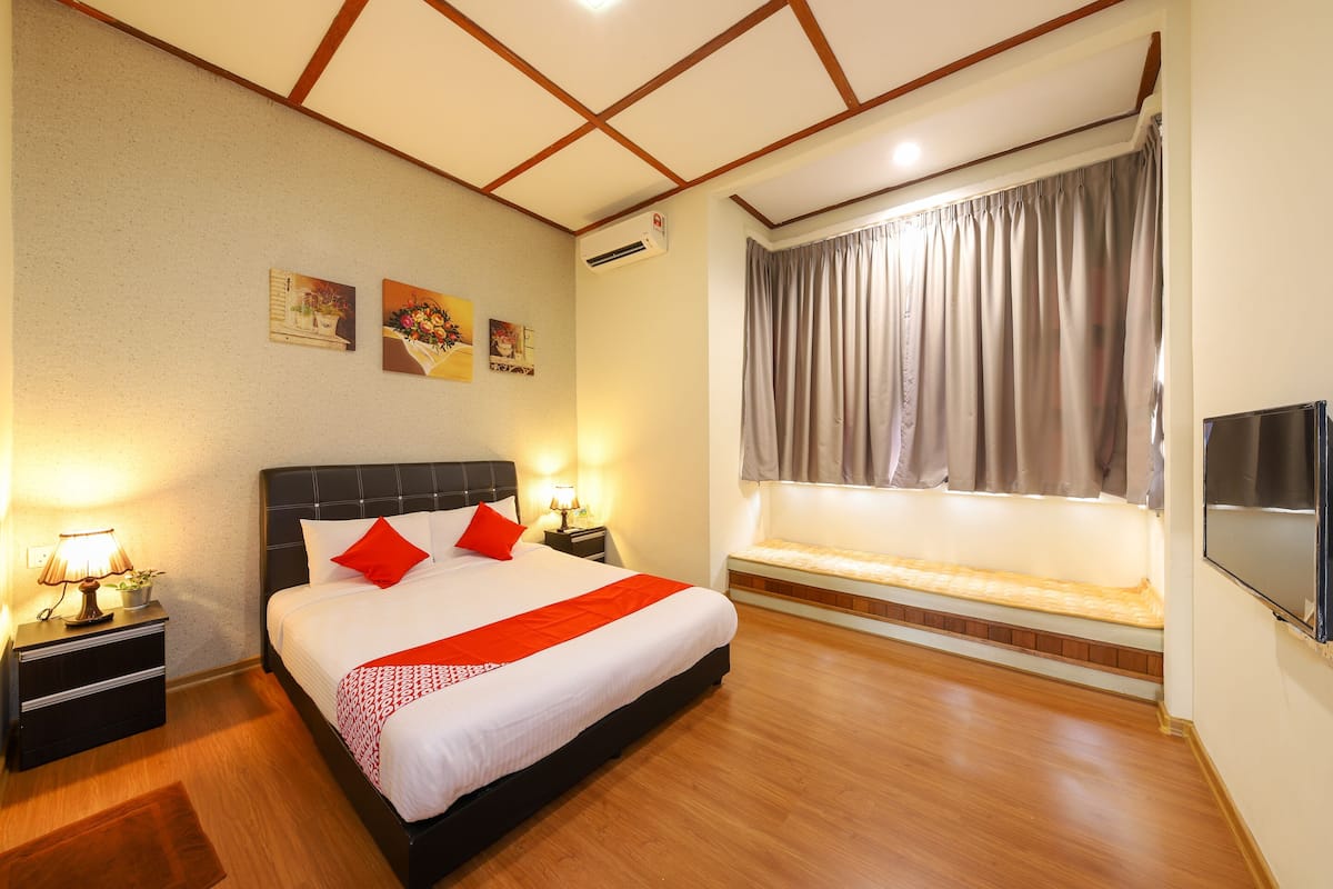 A hotel room with a large bed, bedside tables with lamps, a window with curtains, and a flat-screen TV.
