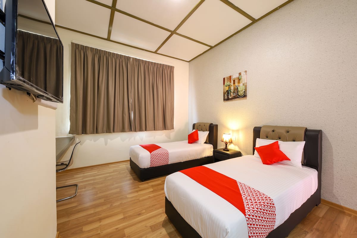 A hotel room with two beds, a TV, a window with curtains, a painting on the wall, and a wooden floor.