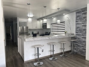 Uma cozinha moderna com bancada de mármore, eletrodomésticos de aço inoxidável e banquetas.