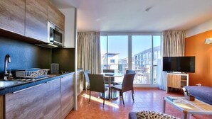 A modern kitchen with a built-in microwave, a dining area with chairs, a flat-screen TV, and a sofa. - Apartment Port Prestige (Antibes)
