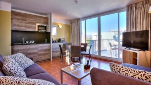A modern living room with a sofa, a coffee table, and a TV. There is a balcony with a view of the city. - Apartment Port Prestige (Antibes)