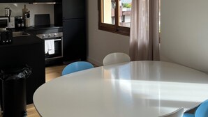 Ett modernt kök med svarta skåp, en inbyggd ugn och en matplats med ett vitt bord och blå stolar.