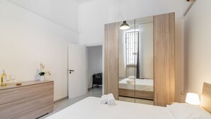 A modern hotel room with a large bed, a wooden wardrobe, a bedside table with a lamp, and a small potted plant. - GuestHost - Functional apartment ideal for two people and equipped with the main services for a comfortable stay. The flat is located 7 minutes walk from the Central Station and 10 minutes from the Aldo Moro University and the Petruzzelli Theater, in an  (Bari)