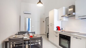A modern kitchen with a dining table, chairs, a refrigerator, an oven, and a pendant light.