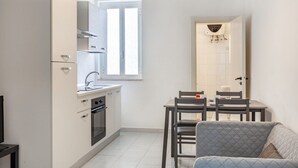A compact kitchen with a window, a dining area with chairs, and a sofa.