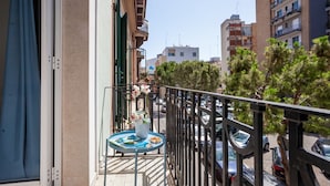 A balcony with a table, railing, and a view of parked cars and buildings.