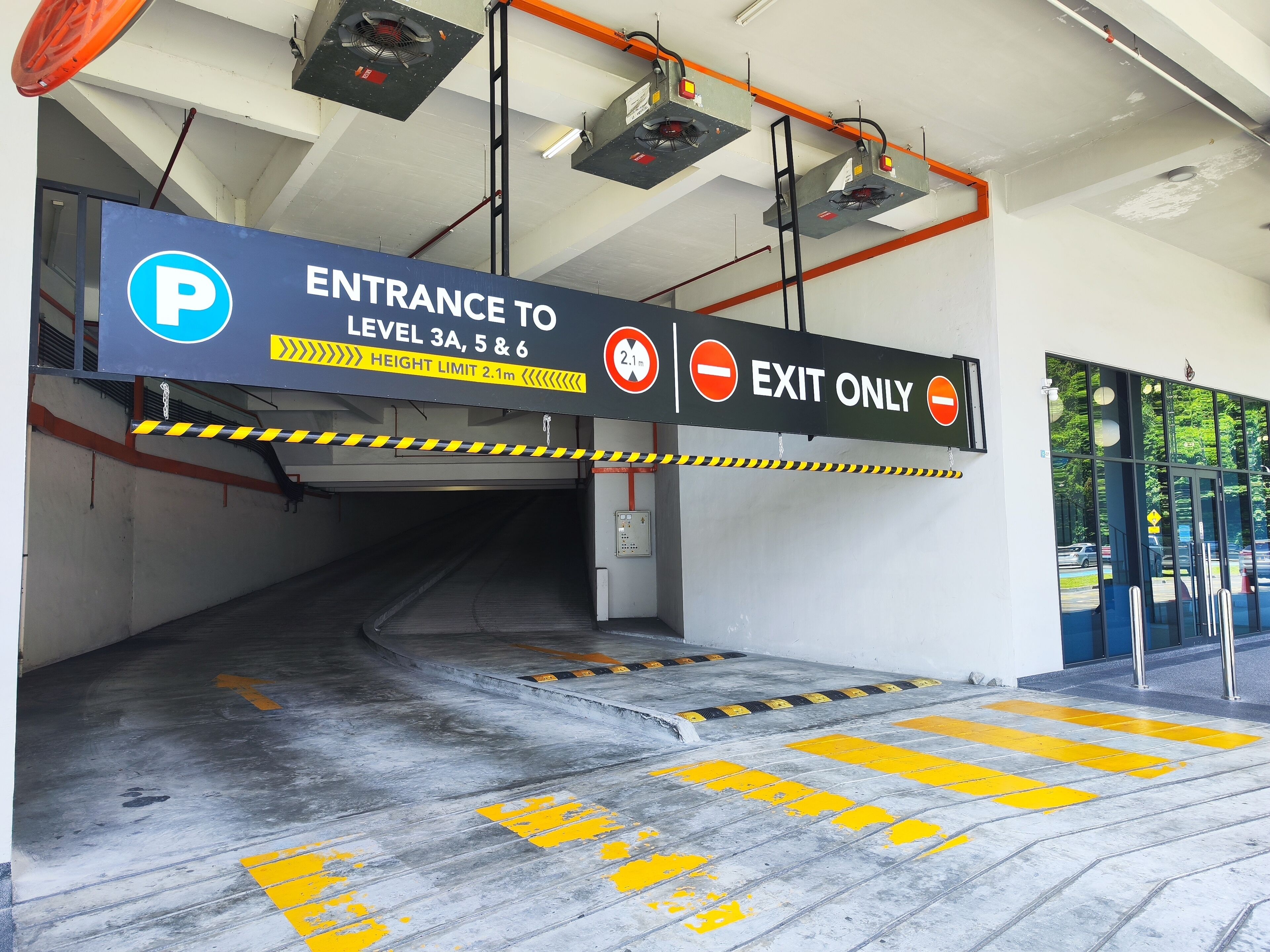 An entrance to a parking garage with a height limit sign, exit-only sign, and yellow tactile paving on the floor.