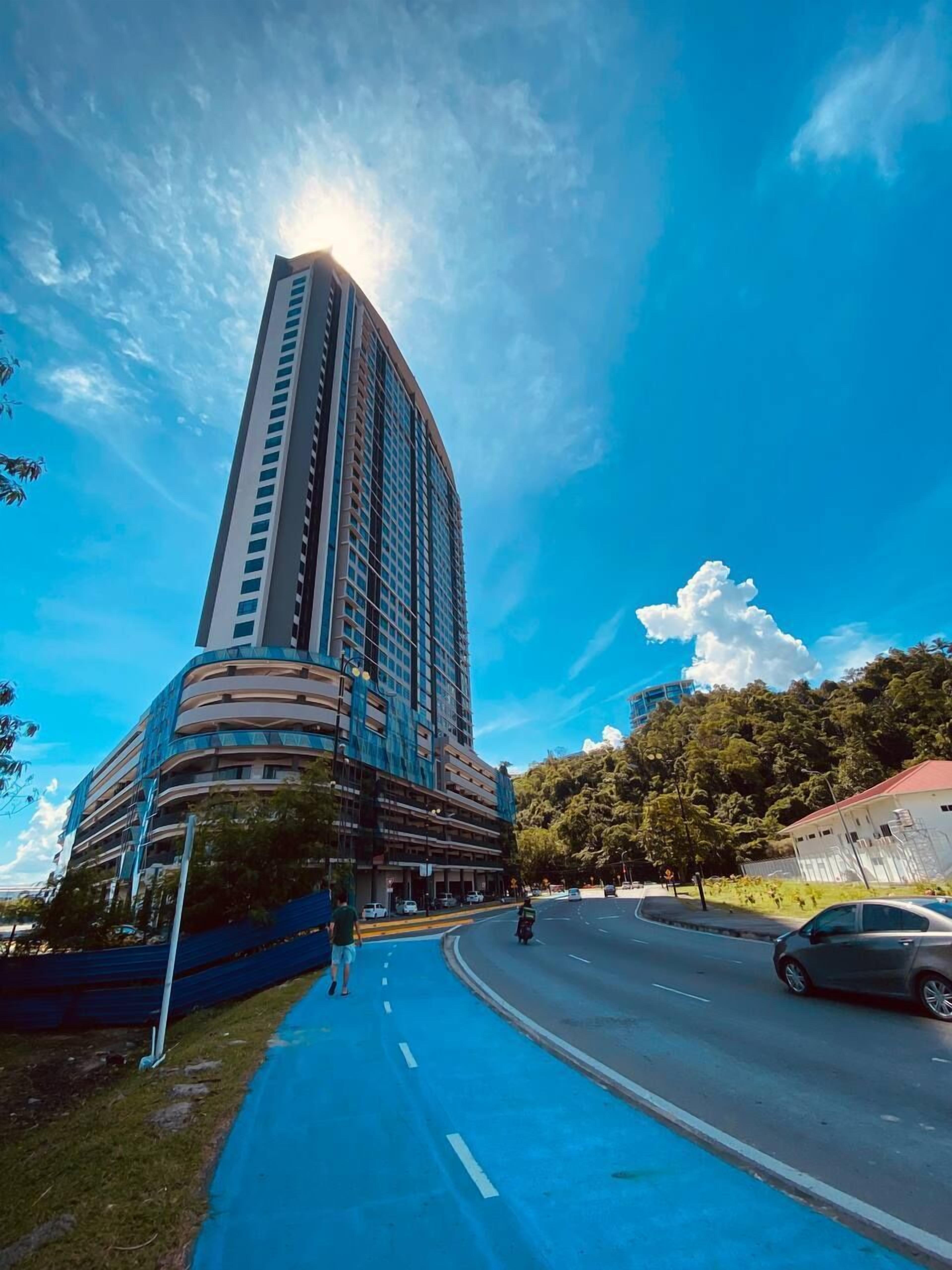 A tall building with a curved facade, a blue pedestrian path, and a clear sky.