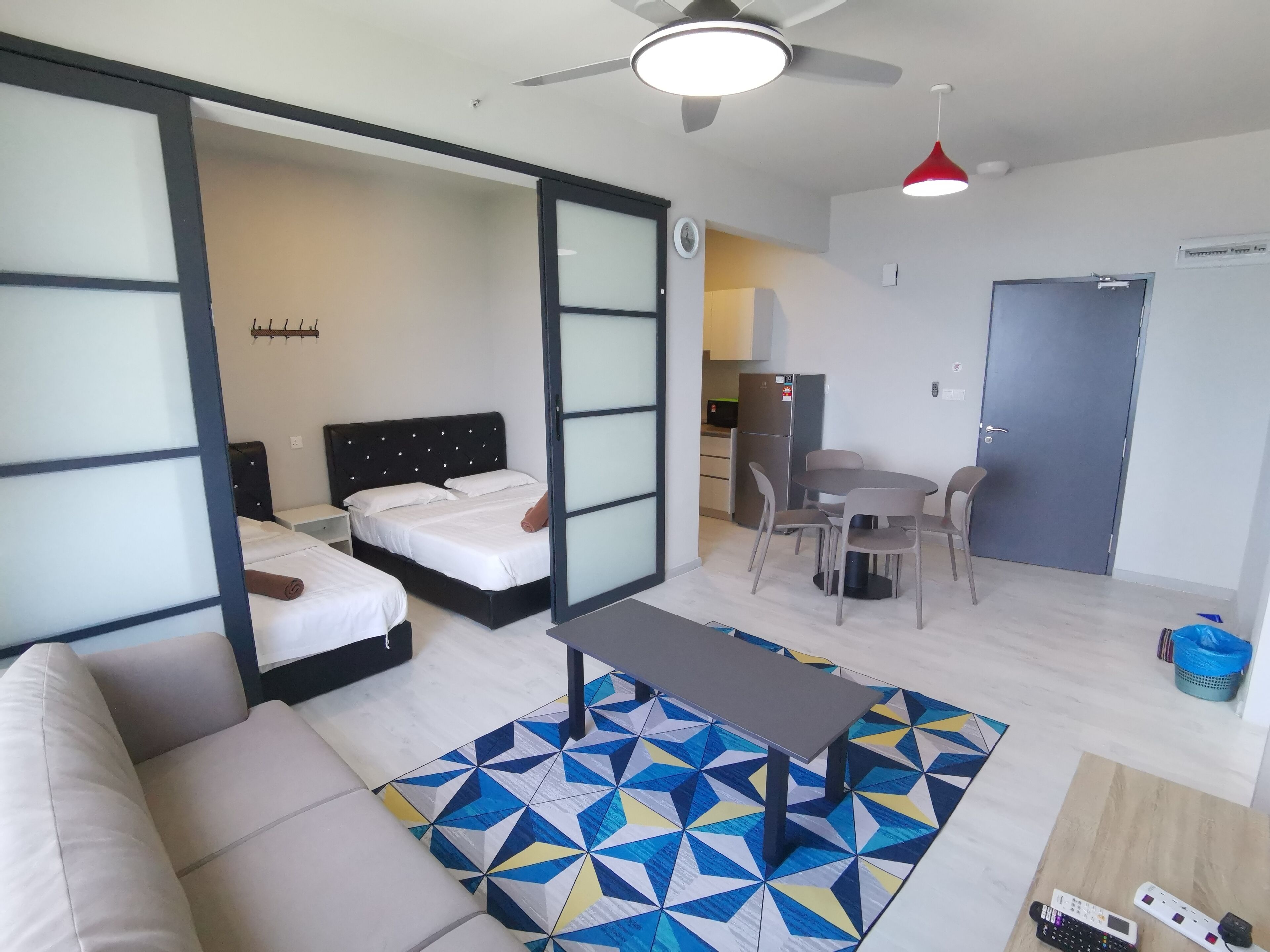 A modern hotel room with a bed, a sofa, a dining table, and a kitchen area.