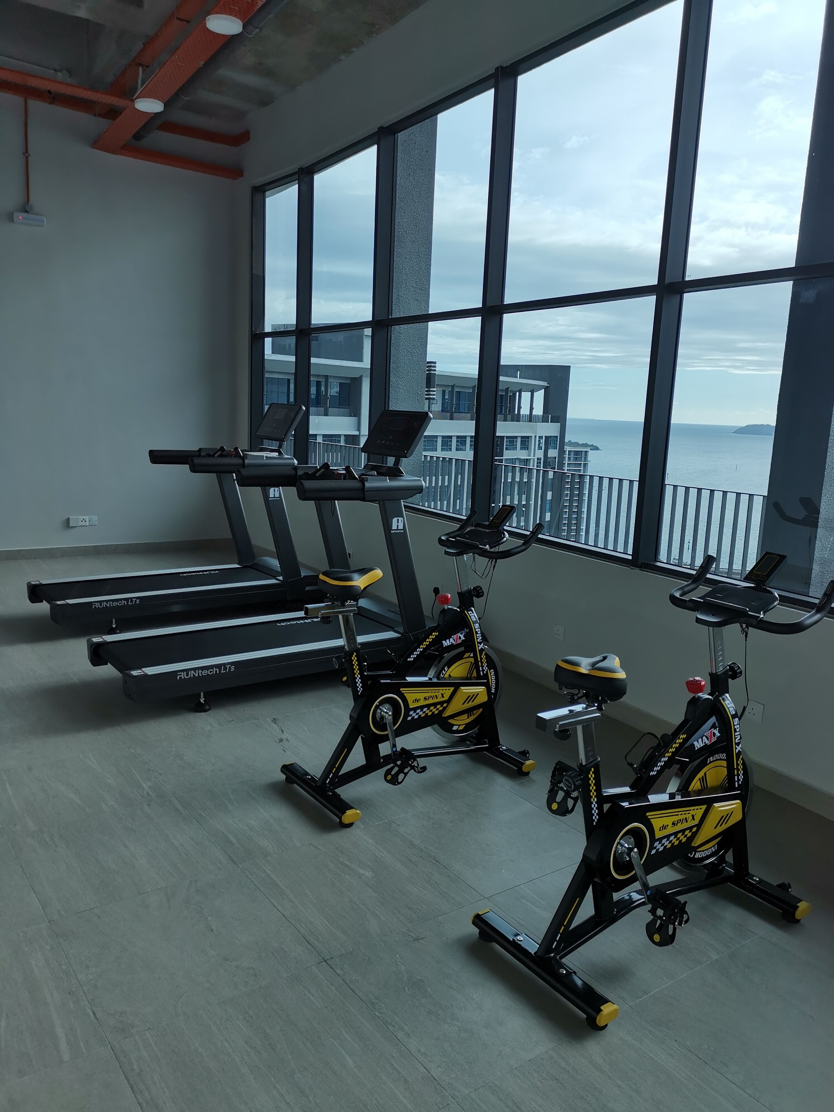 A gym with treadmills, stationary bikes, and a large window offering a view of the sea.