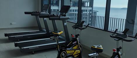 A gym with treadmills, stationary bikes, and a large window offering a view of the sea.