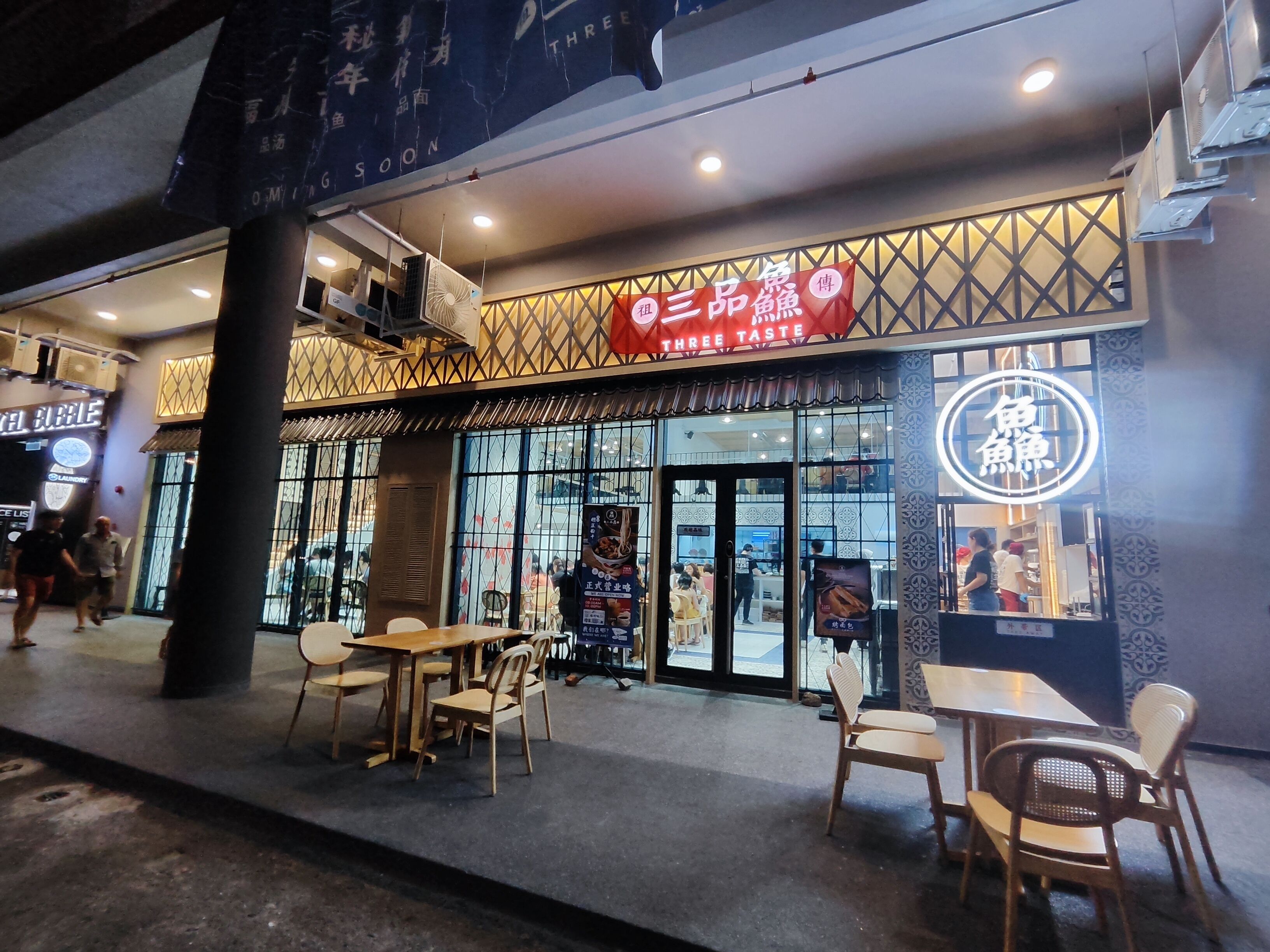Un restaurante con un letrero que dice "Three Taste" y mesas al aire libre.