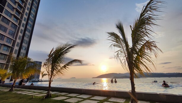 A waterfront swimming area with palm trees and a sunset in the background.