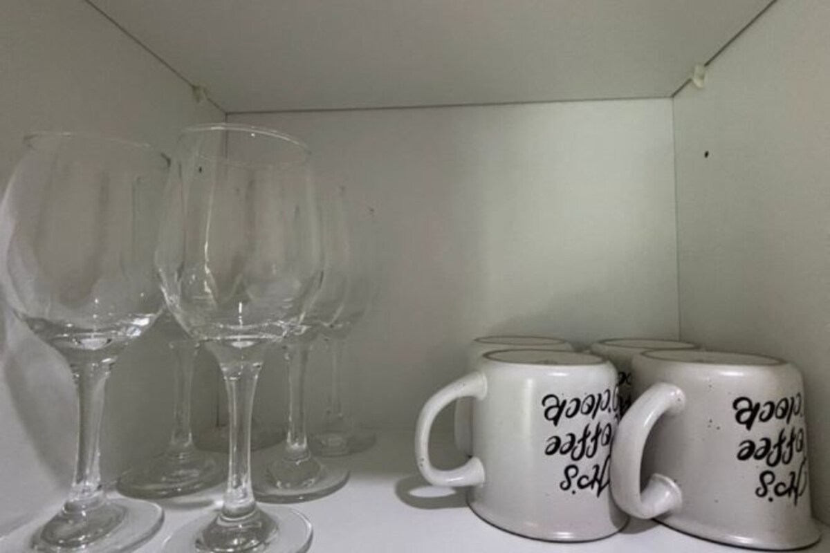 A shelf with wine glasses and white mugs with text.