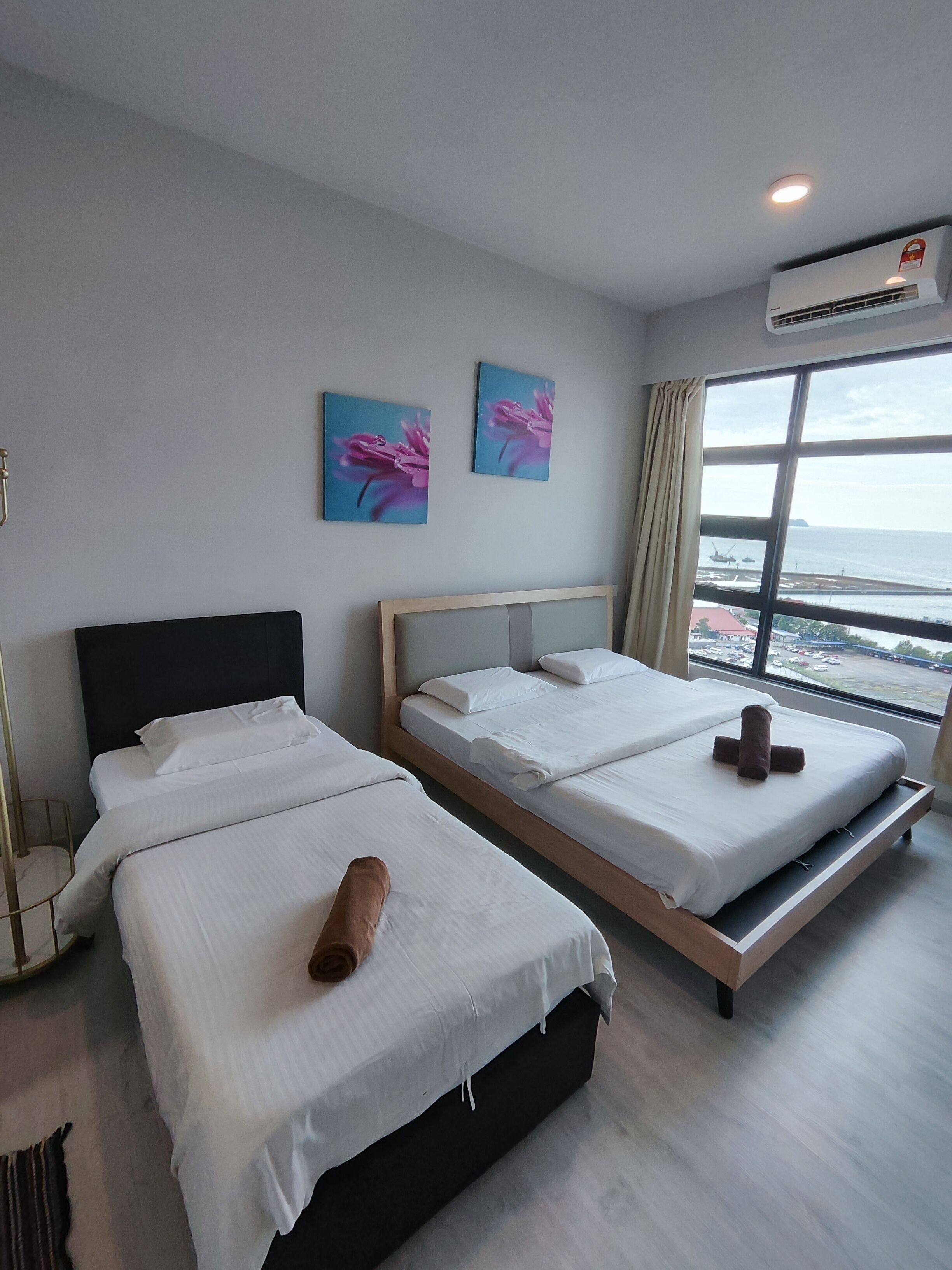 Een hotelkamer met twee bedden, een groot raam met uitzicht op zee, en een airconditioning.