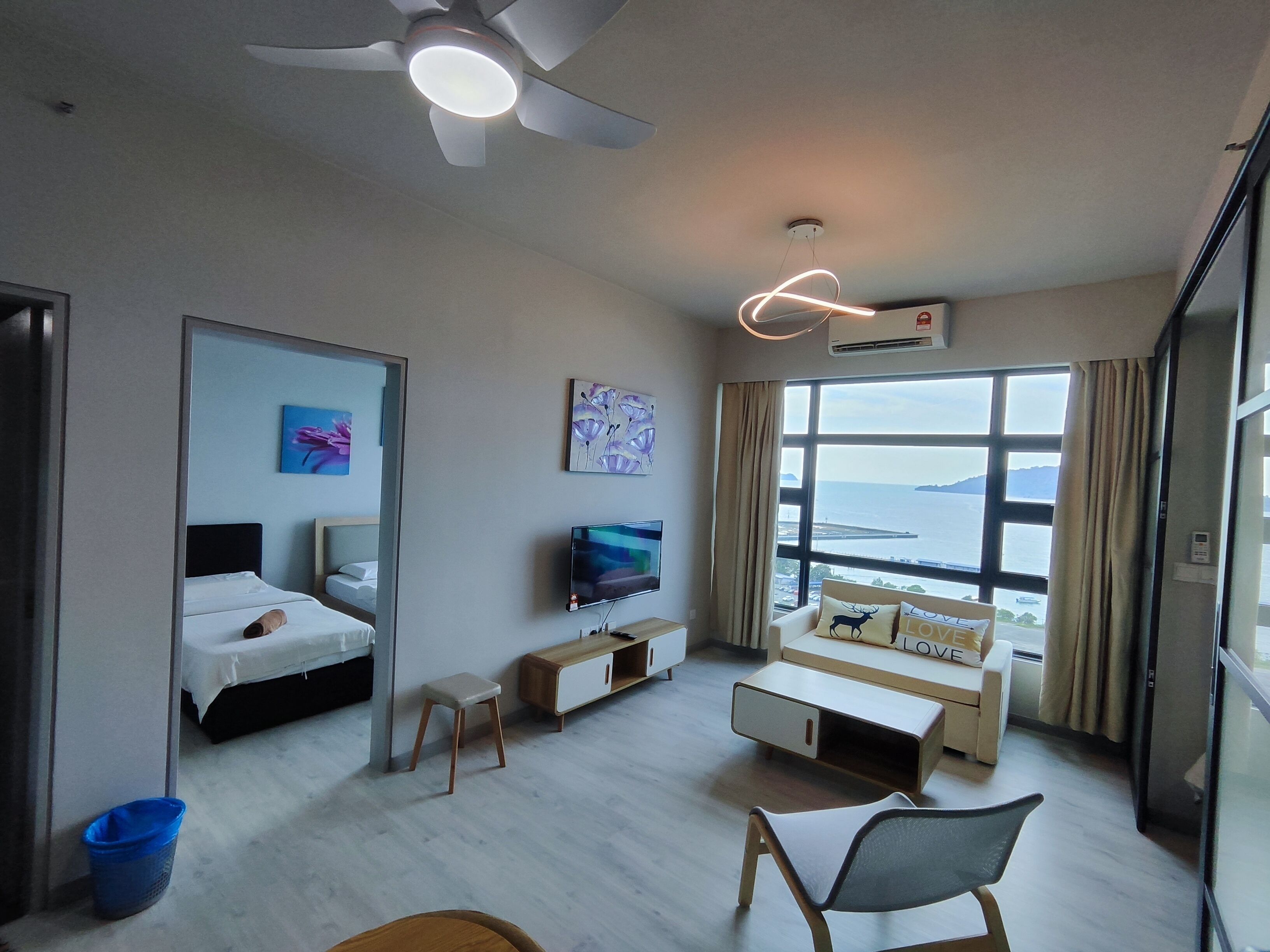 Ett hotellrum med en säng, en TV, en soffa, en takfläkt och ett stort fönster med utsikt över havet.