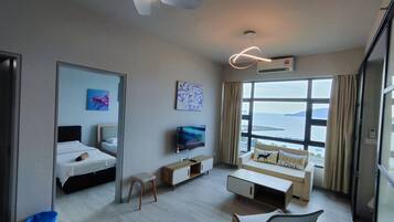 Ett hotellrum med en säng, en TV, en soffa, en takfläkt och ett stort fönster med utsikt över havet.