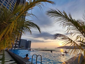 Una piscina con persone, palme e un tramonto sullo sfondo.