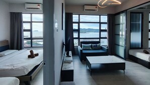 A modern hotel room with two beds, a sofa, a TV, and large windows offering a city view.