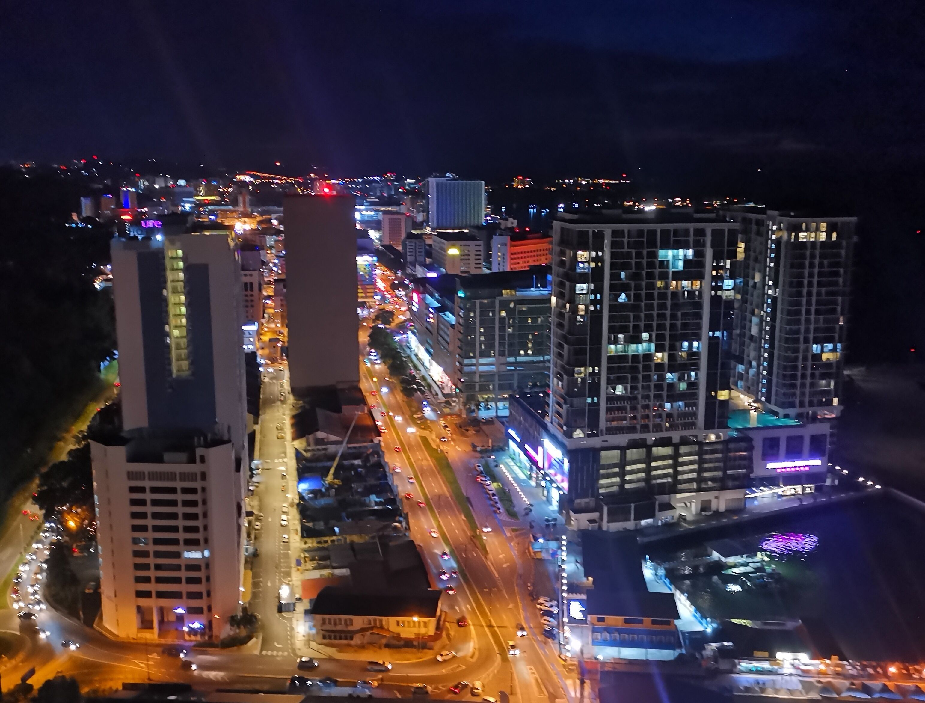 Uma paisagem urbana noturna com edifícios altos, ruas movimentadas e letreiros iluminados.