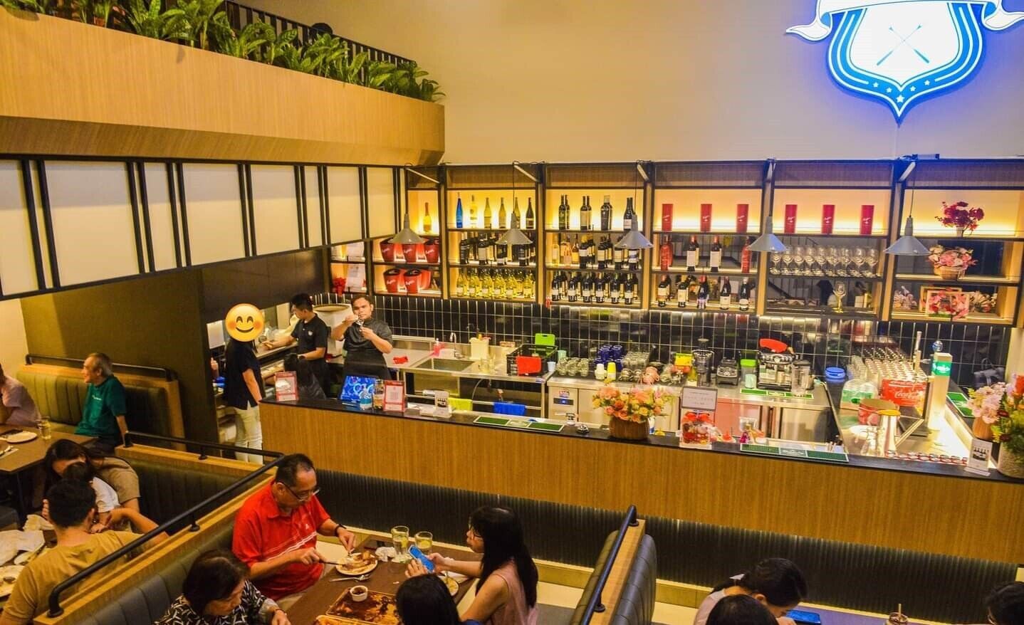 Un restaurante con zona de bar, mesas y sillas, y una variedad de alimentos y bebidas a la vista.
