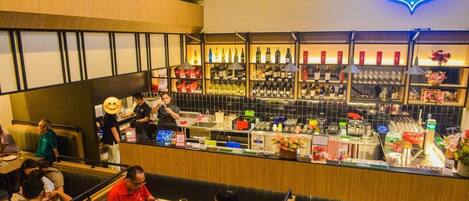 Un restaurante con zona de bar, mesas y sillas, y una variedad de alimentos y bebidas a la vista.