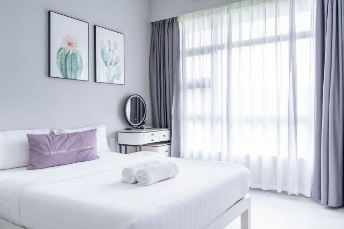 A neatly made bed with white linens and a rolled towel, a bedside table with a mirror, and two framed cactus paintings on the wall.