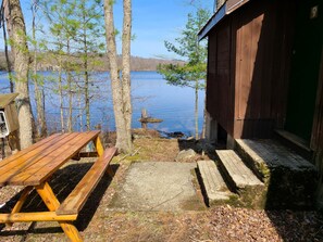 Un banc en bois et une table de pique-nique au bord d’un lac, avec un chalet en bois en arrière-plan.
