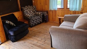 Ein gemütliches Zimmer mit Holzwänden und -böden, ausgestattet mit einem schwarzen Sofa, einem gemusterten Sessel und einem beigen Sofa.