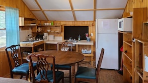 Eine Holzhütte mit einer Küche, einem Esstisch, Stühlen, einem Kühlschrank und verschiedenen Küchengeräten.